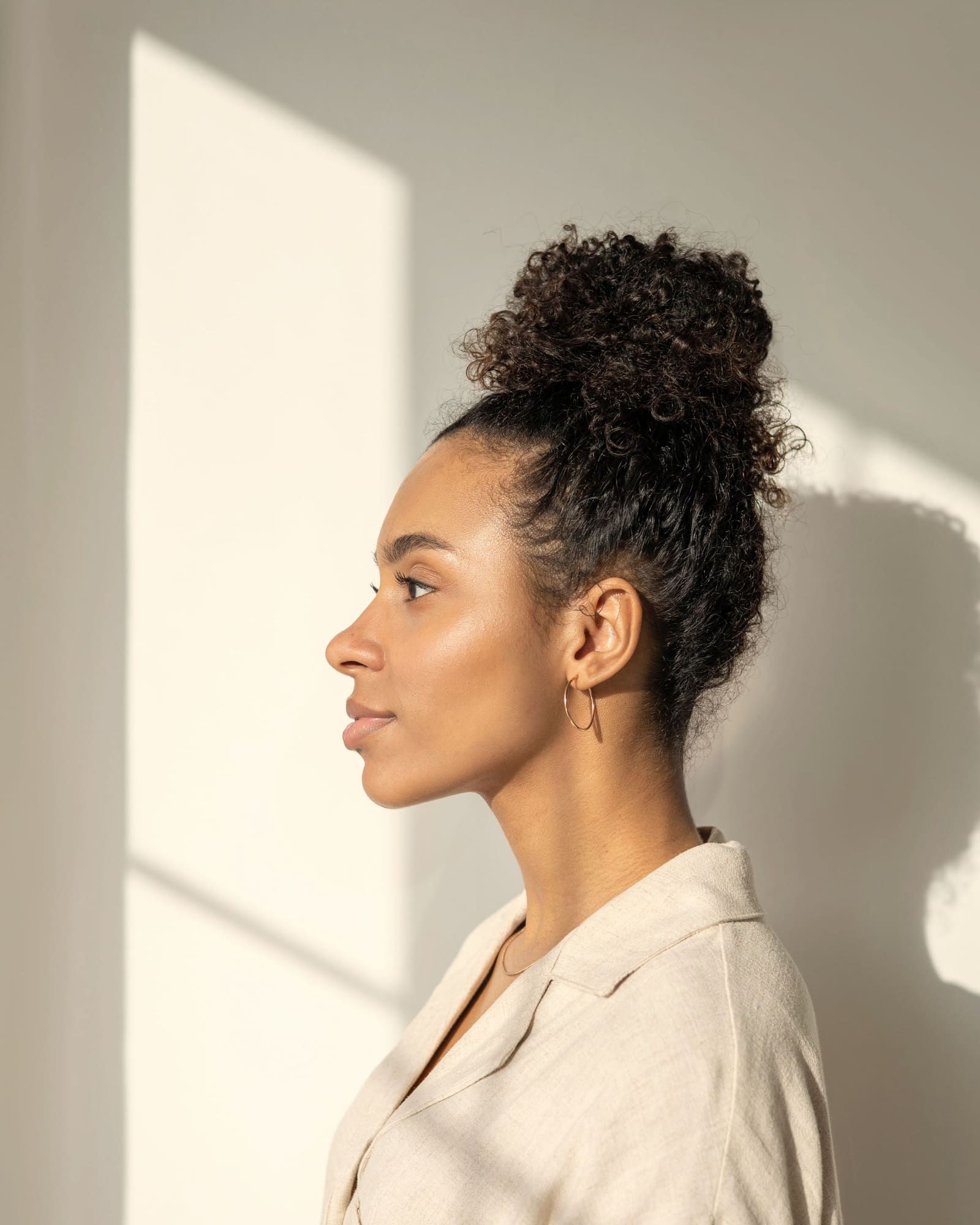 Perfil de uma mulher junto a uma parede clara, com luz do dia